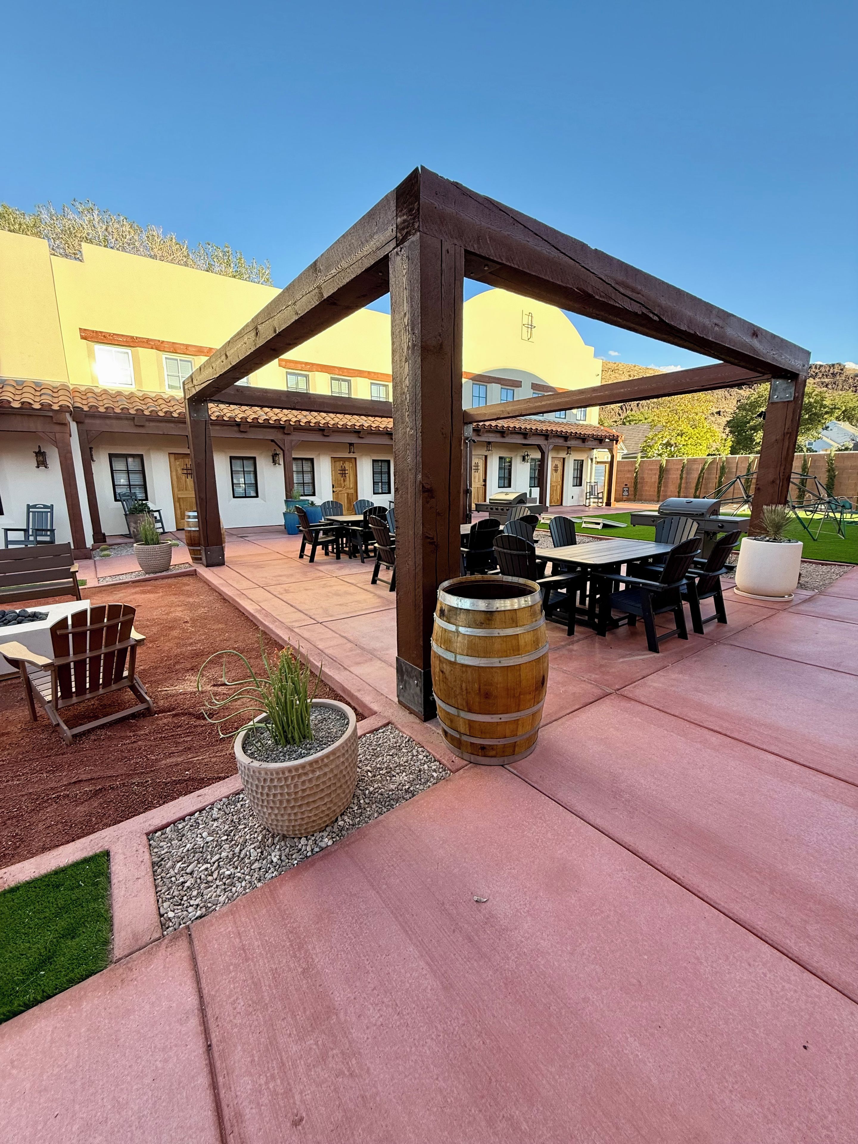 Un patio al aire libre con una pérgola de madera, arreglos de asientos y una parrilla de barbacoa.