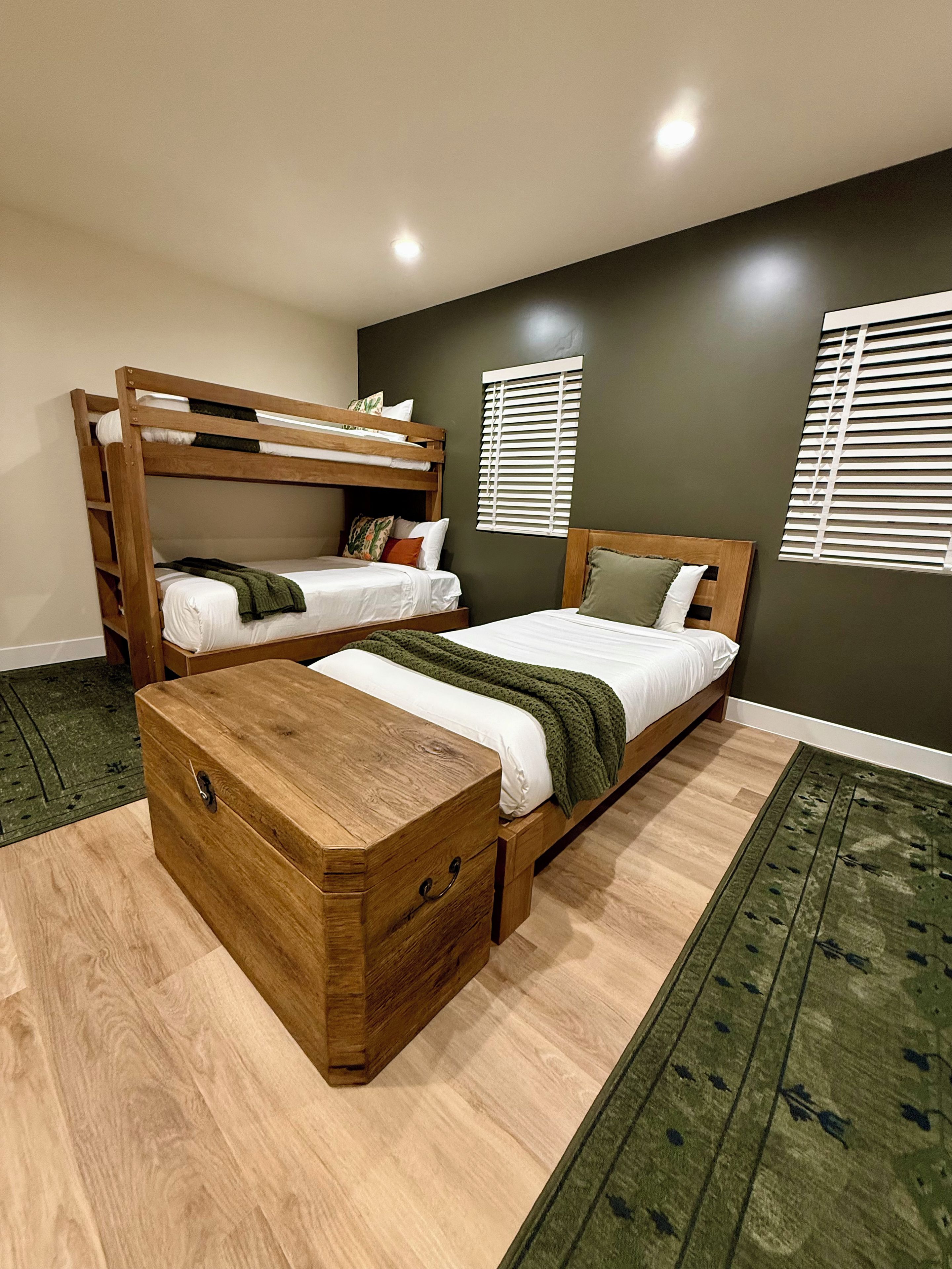 Una habitación con dos literas, un aparador de madera y una alfombra verde estampada.