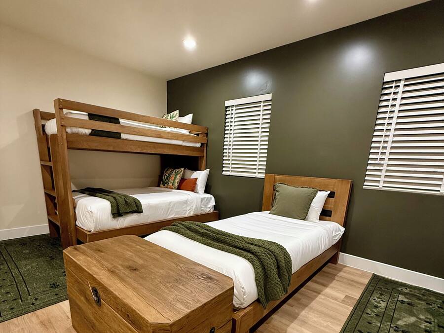 Una habitación con dos literas, un aparador de madera y una alfombra verde estampada.
