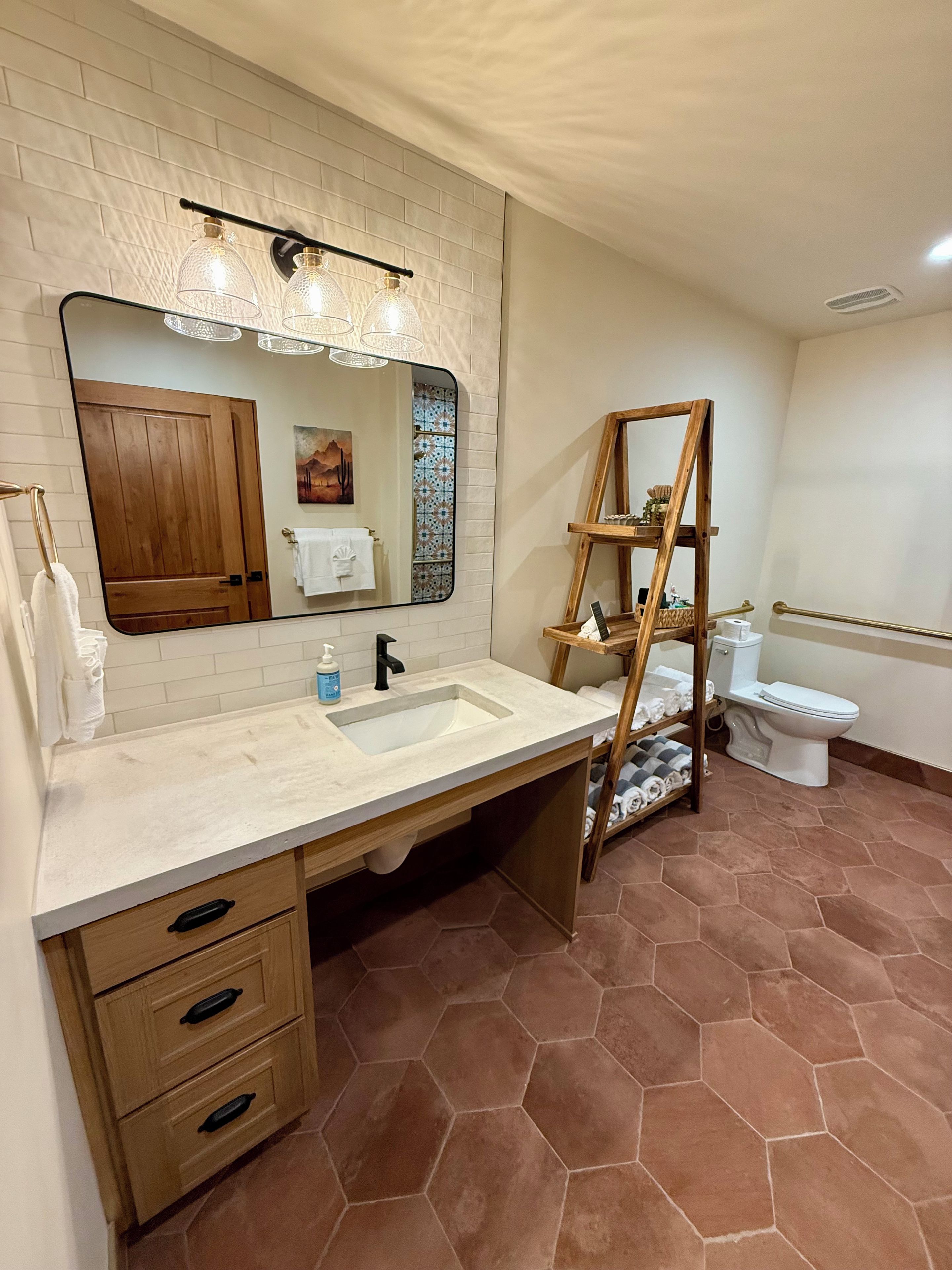 Un baño con lavamanos blanco, tocador de madera, un espejo grande y un estante escalonado de madera.