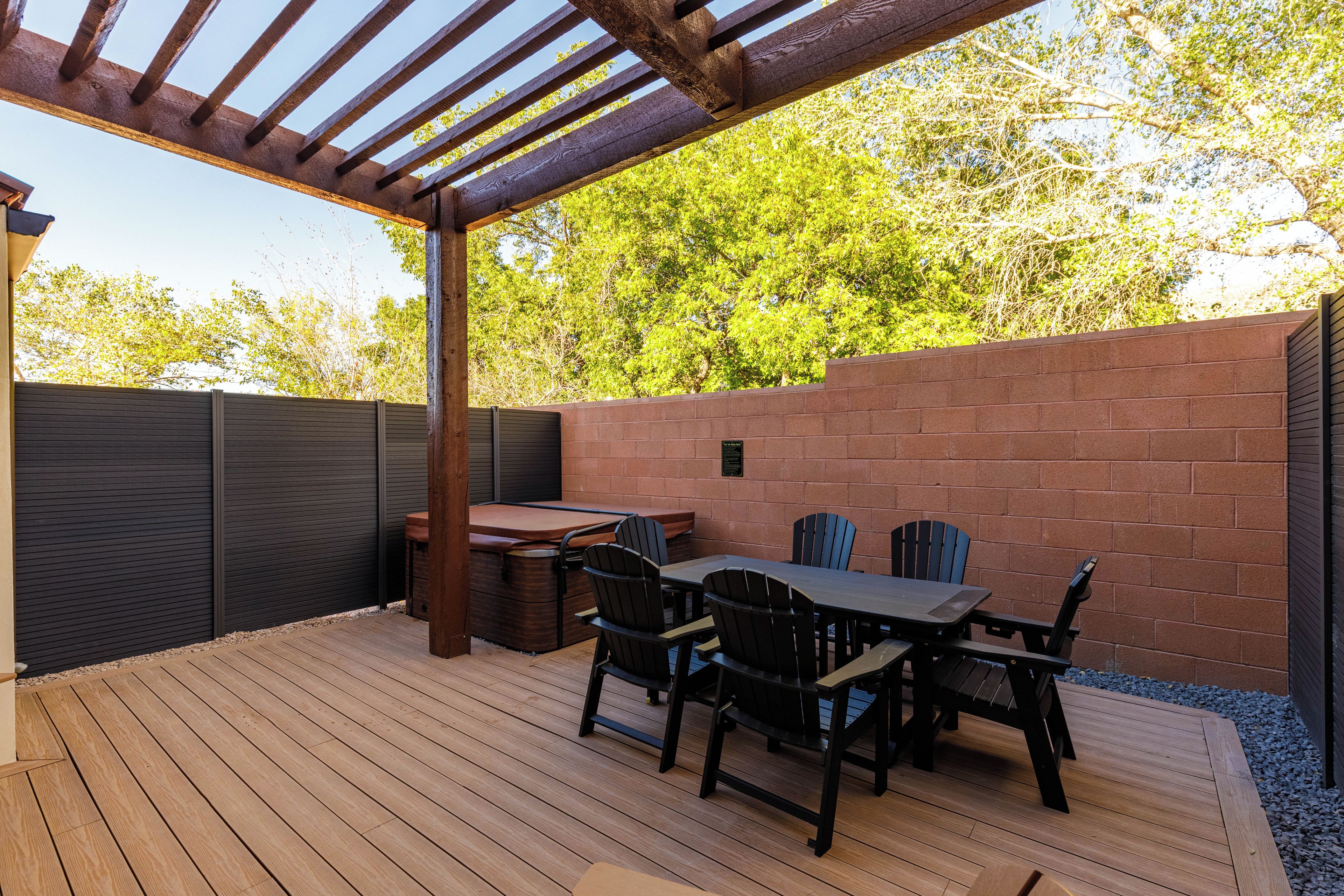 Un patio exterior con terraza de madera, una mesa con sillas, un jacuzzi y un muro de ladrillo.