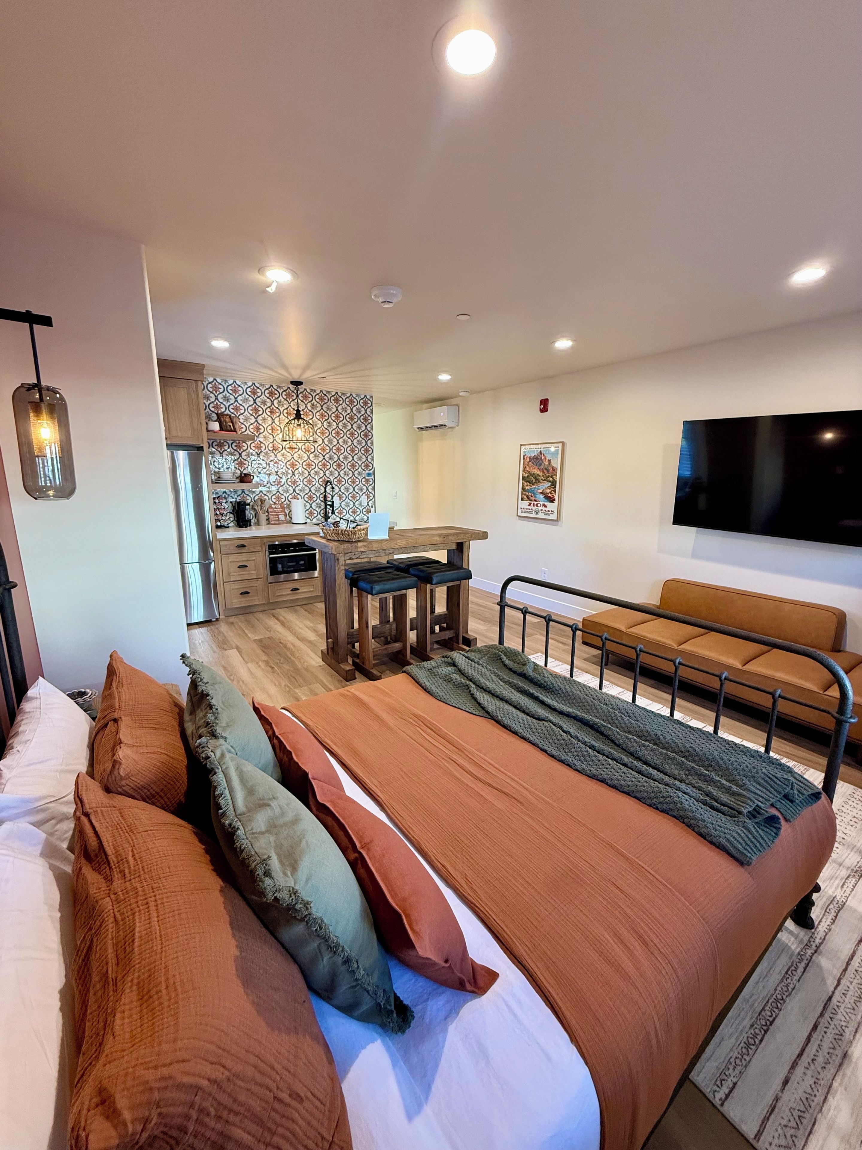 Un dormitorio moderno con una cama grande, un sofá, un televisor y una cocina al fondo.