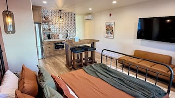 Un dormitorio moderno con una cama grande, un sofá, un televisor y una cocina al fondo.