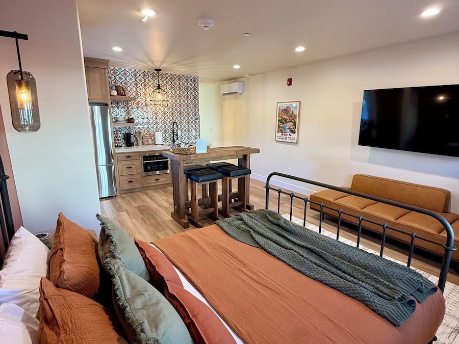 Un dormitorio moderno con una cama grande, un sofá, un televisor y una cocina al fondo.