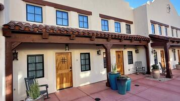 A building with multiple doors and windows, a covered patio area with potted plants, and a clear blue sky.