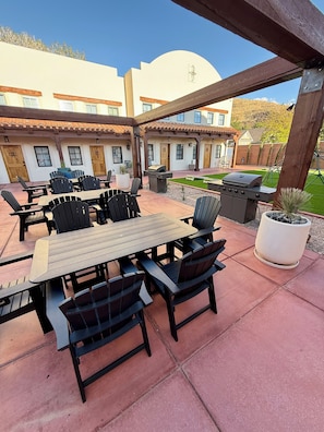 Eine Terrasse im Freien mit Tisch, Stühlen, einem Grill und einem Blumentopf.