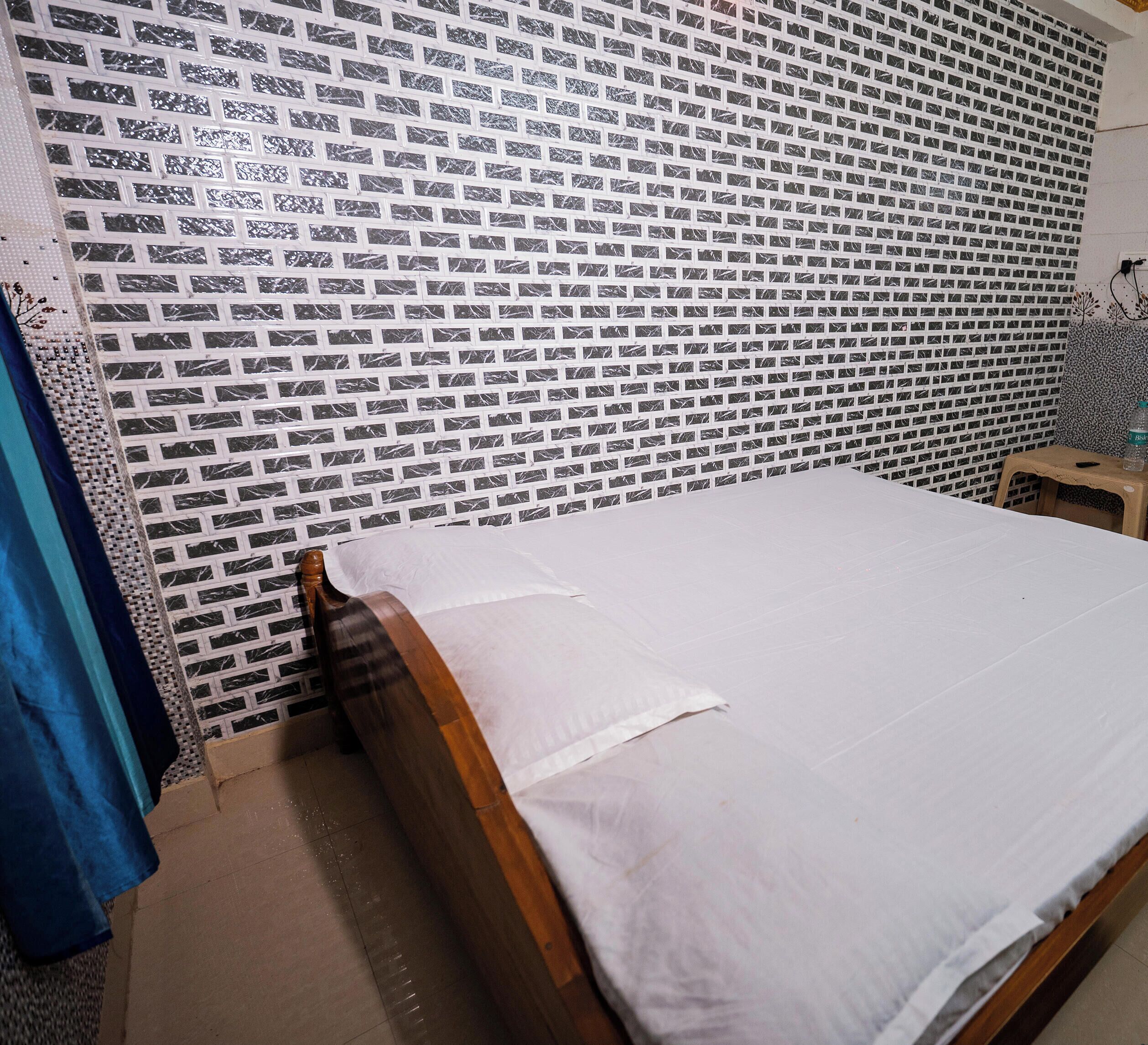 Ein Zimmer mit einem Bett, einer Wand mit Muster, einem kleinen Hocker und einem Vorhang.
