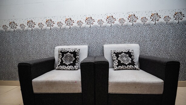 A dark-colored sofa with floral-patterned cushions against a wall with a leaf and tree design. - Hotel Sriram Guest House OD (Puri)