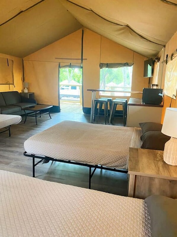 A tented accommodation with a bed, sofa, and table.