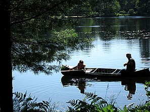 A calm lake with a boat carrying two people. - All Season Romantic One-Room Cabin on Moody Pond, in Upstate New York (Saranac Lake)