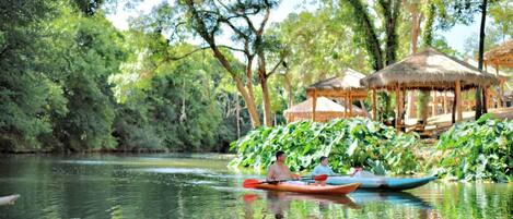 A calm river with a thatched-roof structure and lush greenery.