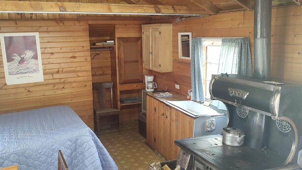 A cabin with a bed, a wooden cabinet, a stove, and a window with curtains.