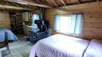 A cabin-style room with two beds, a kitchenette, a stove, and a window with curtains.