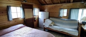 Ein Zimmer in einer Holzhütte mit einem Bett, einer Couch, einem Kühlschrank und einer Tür.