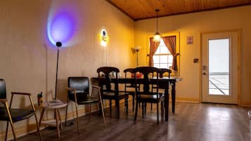 Una habitación con techo de madera, una mesa de comedor con sillas, una lámpara y una puerta con ventanal.