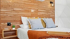 A wooden-paneled bedroom with a bed, pillows, a bedside table, and a nightstand. - Unique Woodland Glamping Dome with Stargazing & Nature Retreat near Wolfe City, TX (Wolfe City)