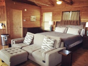 Ein Zimmer in einer Blockhütte mit einer Couch, einem Bett, einer Lampe und einem Papierkorb.