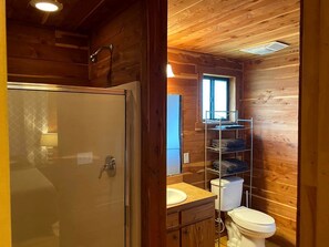 Ein Badezimmer in einer Holzhütte mit Dusche, Toilette und einem Regal mit gefalteten Handtüchern.