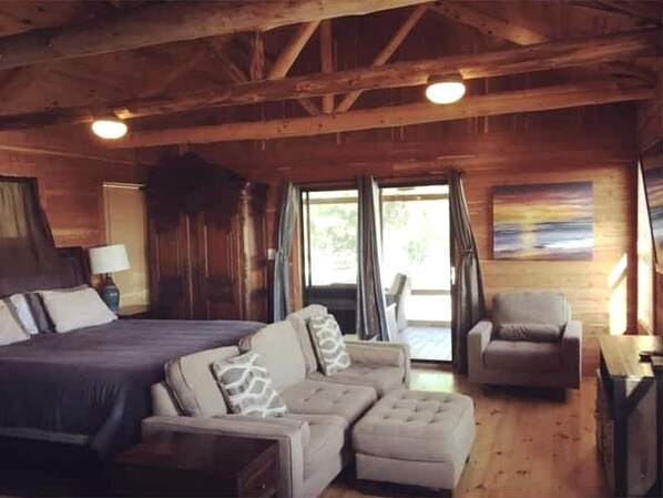 Ein Interieur einer Holzhütte mit Bett, Sofa, Ohrensessel und Tisch.
