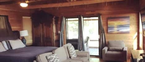 A wooden cabin interior with a bed, sofa, armchair, and a table.