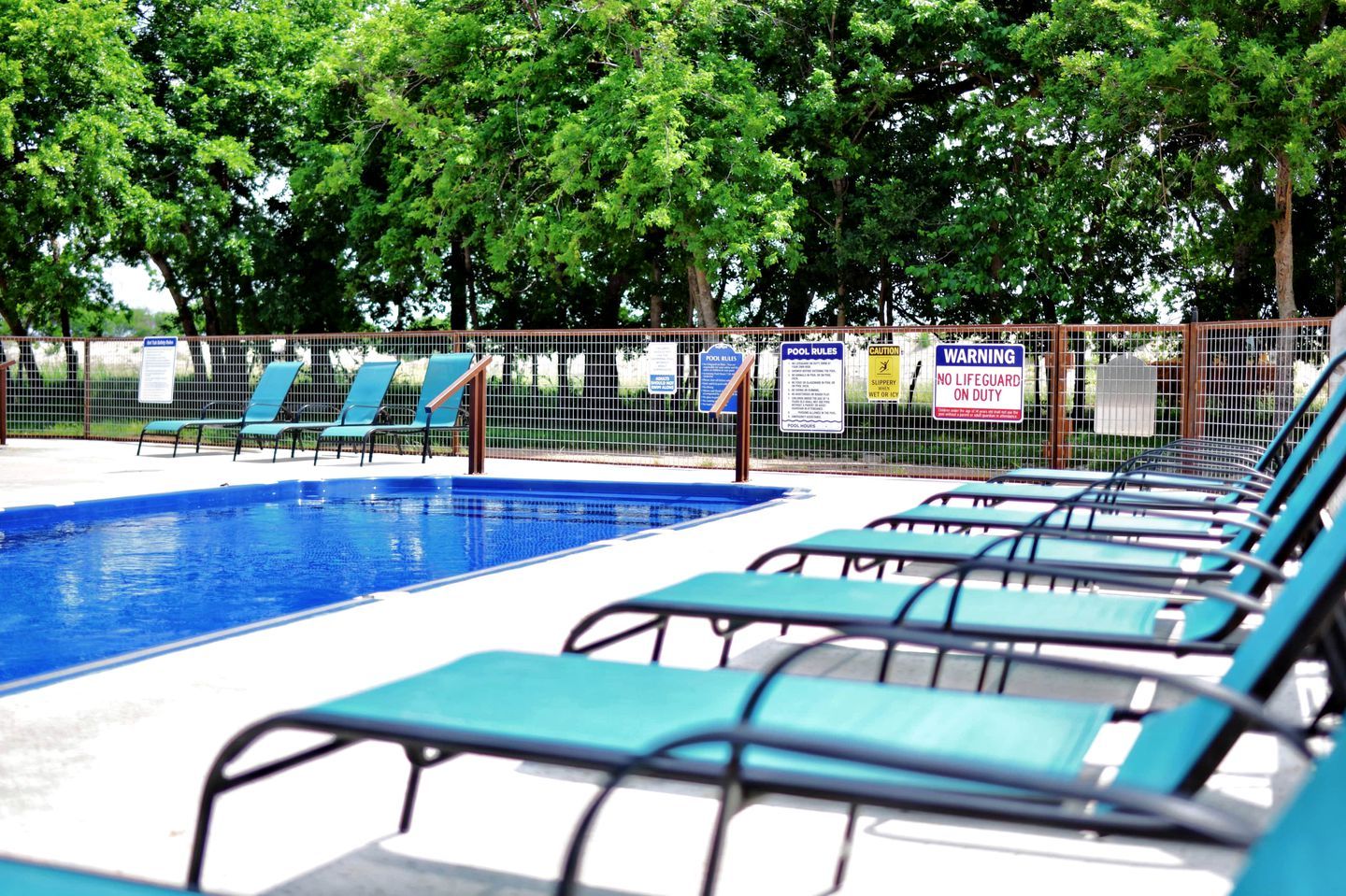 A swimming pool with blue water, surrounded by a fence with lounge chairs.