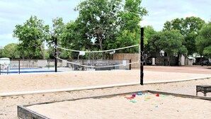 Una cancha de voleibol de arena, con una red, rodeada de árboles y una cerca.