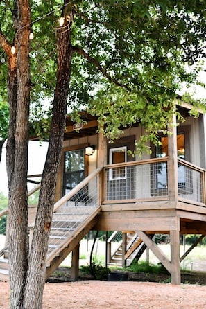 Una casa en el árbol de madera con una escalera y barandilla de metal.