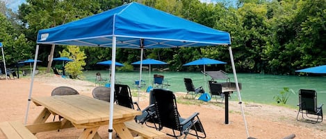Un montaje para picnic en la playa con una mesa, sillas, un toldo y vista al río.