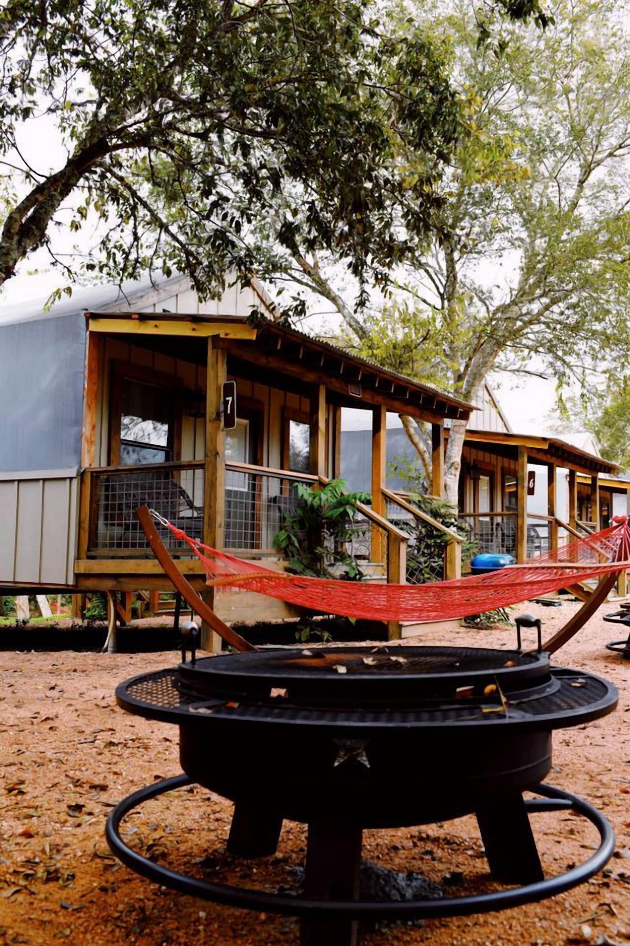 Un espace extérieur rustique comprenant un foyer, un hamac et des structures en bois.