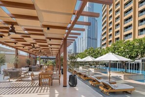 Un área de piscina en la azotea con sillones, pérgolas de madera y vistas a edificios altos.