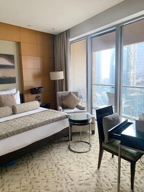 A hotel room with a bed, a chair, a small table, and a large window offering a city view. - Kempinski Central Avenue Residence  (Dubai)