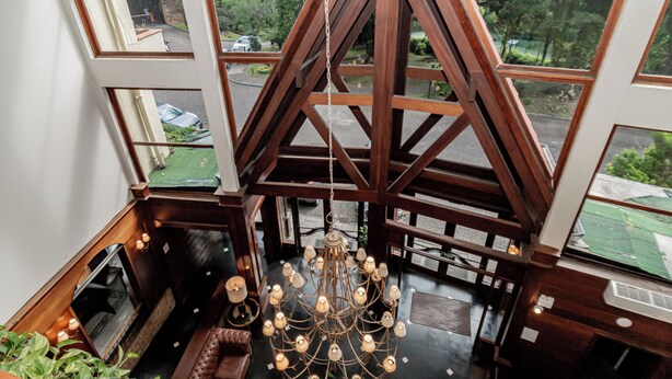 A high-ceilinged room with a chandelier, wooden beams, and large windows offering a view of the street. - Flat in Serrano with full access to the Wish Resort. (Gramado)