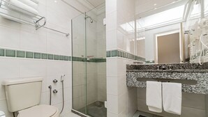 A bathroom with a toilet, a glass-enclosed shower, a sink with a granite countertop, and a mirror. - Flat in Serrano with full access to the Wish Resort. (Gramado)