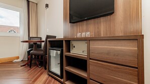 A hotel room with a wooden cabinet, a flat-screen TV, a mini-fridge, a chair, and a table. - Flat in Serrano with full access to the Wish Resort. (Gramado)