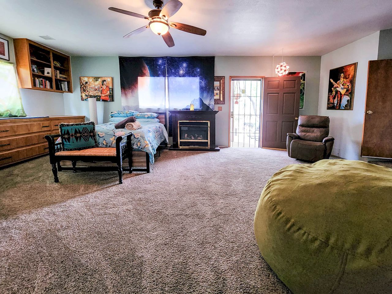 A room with a fireplace, a ceiling fan, a sofa, a chair, and a large window.