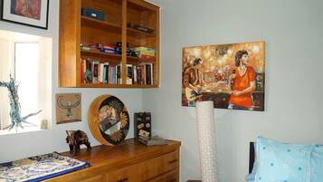 Una habitación con estantería de madera, un cuadro, una lámpara y una cama con ropa de cama estampada.