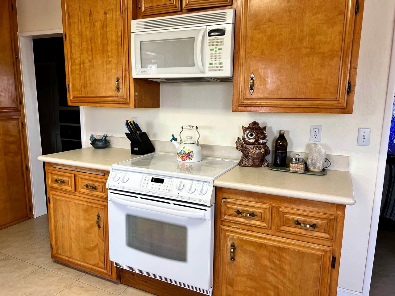 A kitchen with wooden cabinets, a microwave, a stove, and a kettle.