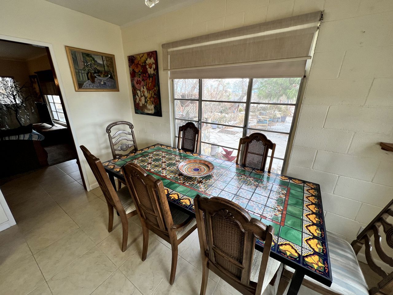 Un comedor con mesa de baldosas, sillas de madera y ventana con vistas.