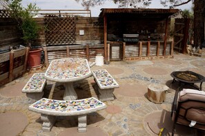 An outdoor patio with mosaic-tiled tables and benches, a barbecue grill, and a wooden fence. - Desert Dreams with Your Furry Friend: Pet-Friendly Rental Under the Stars (Yucca Valley)