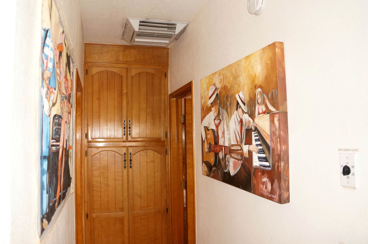 Un pasillo con puertas dobles de madera, un respiradero en el techo y un cuadro de músicos en la pared.