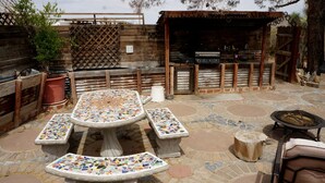 Eine Terrasse im Freien mit mozaikbesetzten Tischen und Bänken, einem Grill und einem Holzzaun.