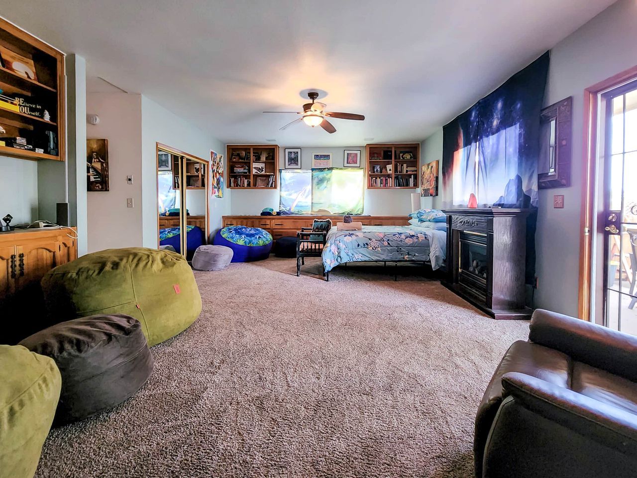 A living room with a fireplace, bean bags, a bed, and a ceiling fan.