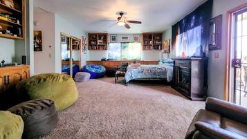 A living room with a fireplace, bean bags, a bed, and a ceiling fan.