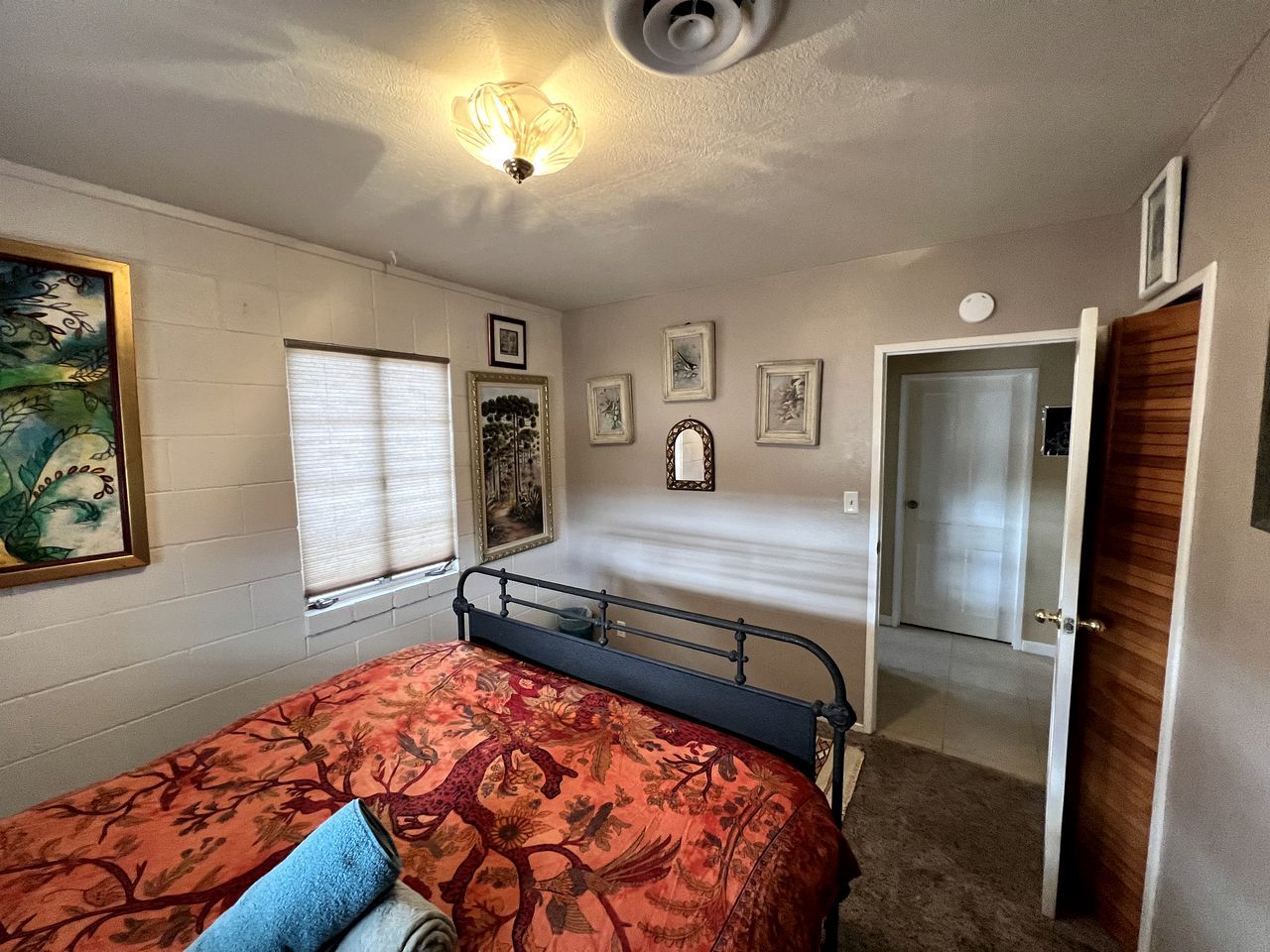 A bedroom with a bed, a window with blinds, a door, and a wall-mounted light fixture.