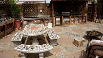 An outdoor patio with mosaic-tiled tables and benches, a barbecue grill, and a wooden fence.