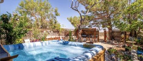 A hot tub surrounded by a wooden deck, with trees and a rustic fence in the background.