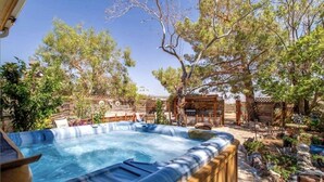 Ein Whirlpool, umgeben von einer Holzterrasse, mit Bäumen und einem rustikalen Zaun im Hintergrund.