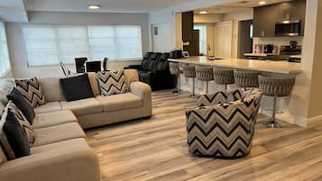 Un salon moderne avec un canapé d’angle, une table basse et un coin bar équipé de tabourets.