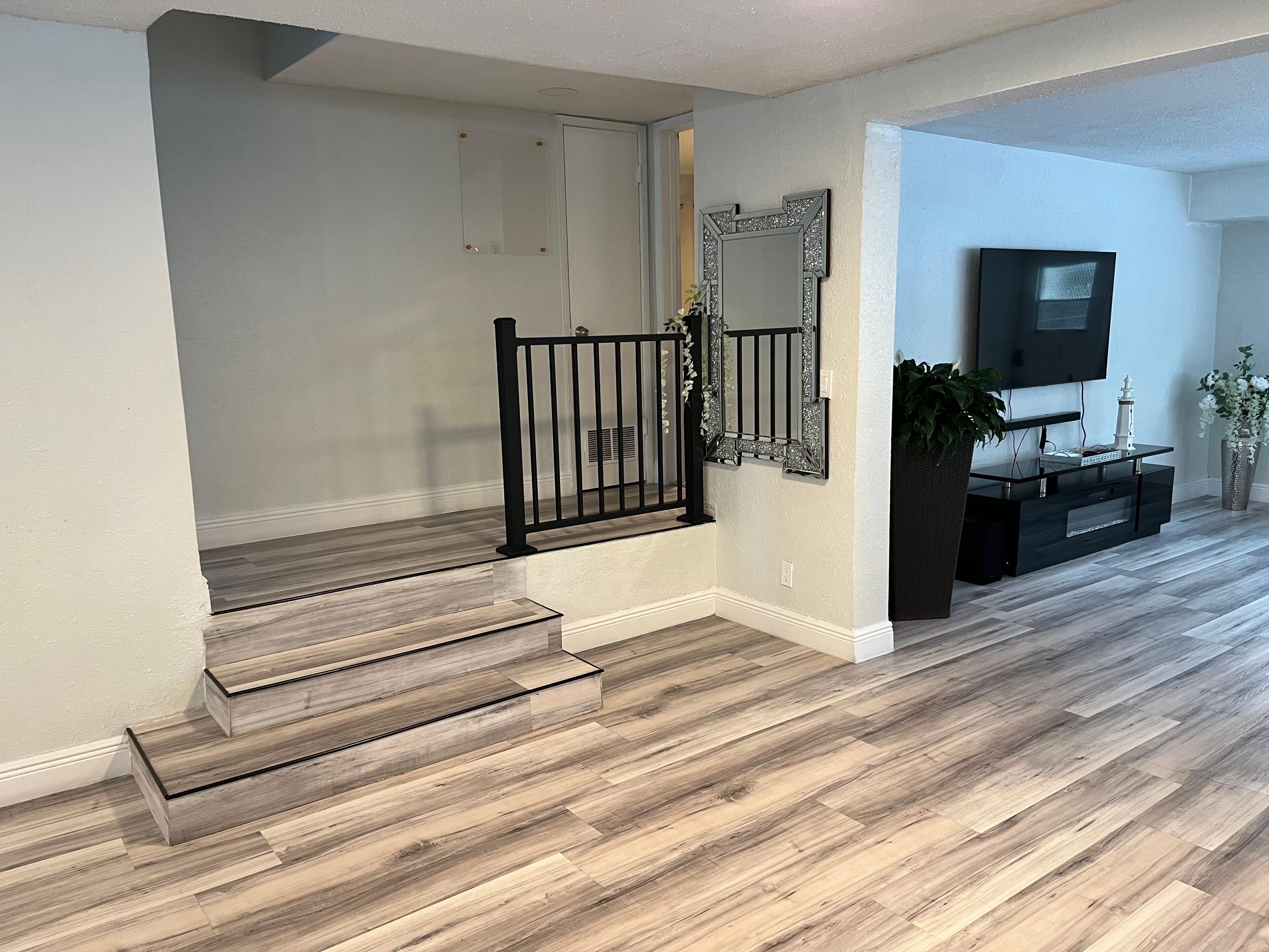 Un escalier avec des marches en bois et des rampes noires, un téléviseur à écran plat fixé au mur et une plante en pot.
