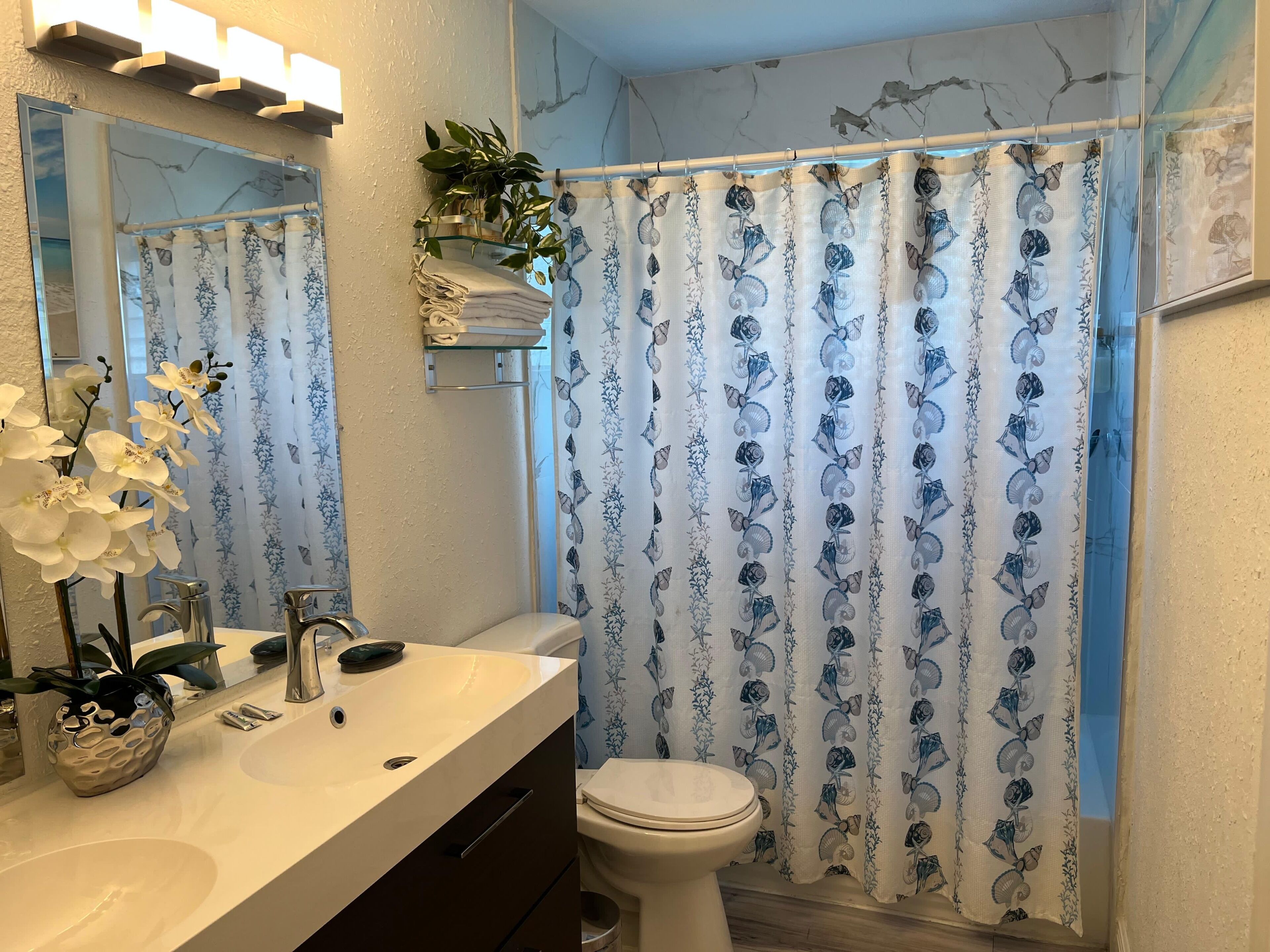 Een badkamer met een wit wastafel, toilet, spiegel en douchegordijn met schelpenprint.